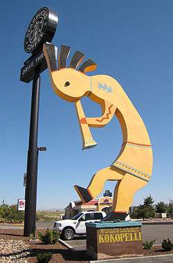 A large yellow statue of a simplified line drawing of Kokopelli playing a flute