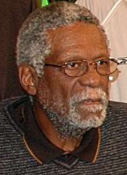 A black bearded elderly man wearing glasses looks toward the right