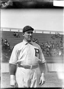 A black-and-white photograph of a man in a white old-style baseball uniform with a dark-colored "P" over the left breast