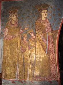 A mustachioed man who wears a crown, with crowned woman and two boys