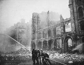 Historical photograph of a building severely damaged by air-raid bombing; firefighters are putting out a blaze in the ruins.