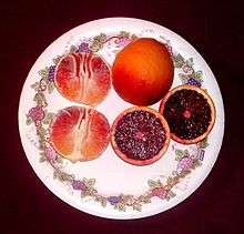 A plate showing three blood oranges:  one whole, one peeled, and one sliced in half