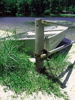 A metal rowboat chained to a metal pole with a lake behind