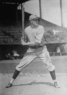 A man wearing a pinstriped old-style baseball uniform and holding a baseball bat over his shoulder