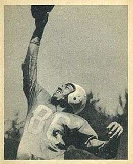 A black and white photo of Bob Mann reaching up with one hand to catch a football