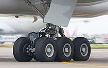 Aircraft landing gear. Six wheel gear on the ground, with attachment assembly and gear door leading up to the aircraft belly.