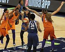 Very tall woman with arms raised, young woman passing the ball forward under strain, surrounded by players