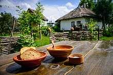 A meal of borscht and bread on a wooden table standing in the yard of a traditional peasant hut
