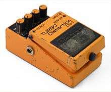 A small effect unit pedal, painted in orange paint that is scuffed from heavy use.
