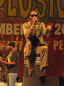 Man with cornrows singing into microphone onstage