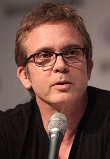 A man wearing a black shirt speaks into a microphone.