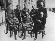 A black and white photograph of eight men, five standing and three seated, most of whom are wearing British military uniforms. The man standing in the middle is believed to be then-Lieutenant Colonel Pink.