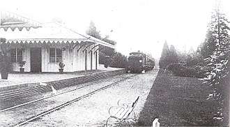 A train on a single rail track near a small white wooden station.