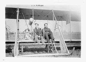 Harry Bingham Brown at the center of an early airplane. On his left sits another passenger.