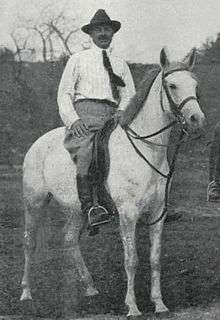 Black and white photo of a man sitting astride a light gray horse