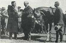 W.R. Brown accepting a silver bowl from another man, with a horse and its rider, dismounted, standing to the right