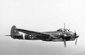 A twin engine propeller powered aircraft in flight and viewed from the right side. The aircraft bears multiple markings including a black and white cross on its side and swastika on the tail fin