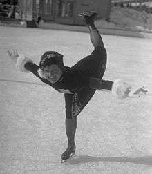 A woman wearing a dress and gloves is skating on an ice rink