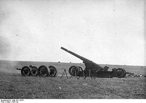 A large gun on its firing plate pointing to left in open ground. A wheeled carriage is nearby.
