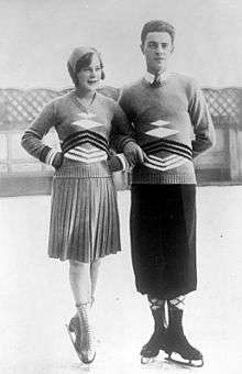 A man and woman standing on an ice rink in figure skates and wearing matching sweaters