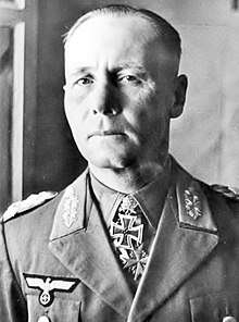 The head and shoulders of an elderly man, shown in semi-profile. He wears a peaked cap and a military uniform with an Eagle above his right and various military decorations above left breast pocket, and an Iron Cross displayed at the front of his shirt collar. His facial expression is a determined; his eyes are looking into the distance to the left of the camera.