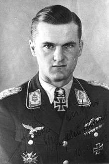 The head and shoulders of a young man, shown in semi-profile. He wears a military uniform with an Iron Cross displayed at the front of his shirt collar.