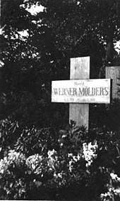 Black-and-white photograph of a wooden cross on a grave, bearing the inscription "Oberst Werner Mölders, 18. 3. 1913&nbsp;– 22. 11. 1944."