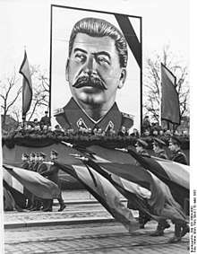 A man with dark hair and moustache, wearing a uniform, posted over a military parade
