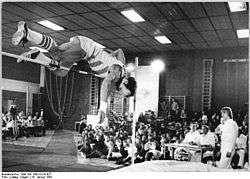 Rolf Beilschmidt jumps over a bar while spectators look on