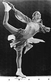 A female figure skater holds up her right leg with her right hand.