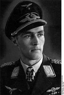 The head and shoulders of a young man, shown in semi-profile. He wears a peaked cap and a military uniform with an Iron Cross displayed at the front of his shirt collar.