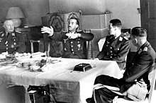 Black-and-white photograph of four men wearing uniforms at a dinner party.