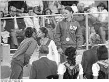 One girl in a track suit with a medal around her neck looks on as two girls congratulate each other