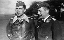 Black-and-white photograph showing half-length view of two uniformed men outdoors, standing next to each other.
