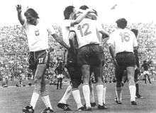 Football players in white shirts and dark shorts celebrate together