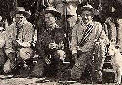Photo taken in 1893 of three Bulawayo field scouts kneeling in front of their horses. Bob Bain on the left, Burnham in the middle, Maurice Gifford and his dog on the right.  Burnham is dressed in his Arizona clothes and is holding his Winchester model 1873 .44WCF rifle