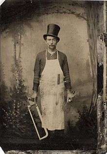 A man wearing an apron and holding two saws