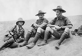 An informal black and white group portrait of three men in military uniform. They are sitting on the ground in what appears to be a desert.