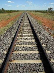straight railway tracks bisect a grassy plain with red soil