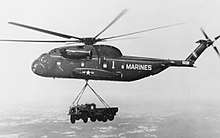 Black and white photograph of a helicopter in flight with a truck slung below it