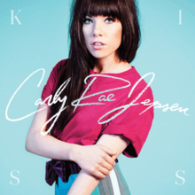 The album cover shows Carly Rae Jepsen against a light blue background. She is photographed from the waist up, holding her left arm with the opposite hand, and is wearing a pink T-shirt. Across the middle of the cover, "Carly Rae Jepsen" is written in white cursive text. The letters of the word "kiss" appear in each corner clockwise in white, all-capital text.