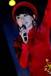 Tiên, in a red long-sleeved top and hat, holding a microphone
