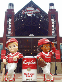 Outside of the stadium with two campbell's mascotts leaning on a campbell's soup can.