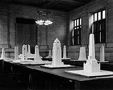 Approximately a dozen monument models sit on tables in a stone-walled room.