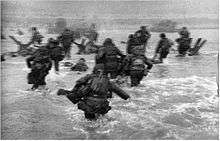 A blurry picture of American men moving through the water to the beach.