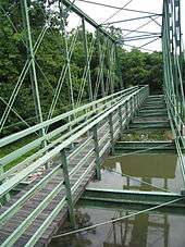 An image of the wooden walkway spanning the length of the green Whipple truss bridge