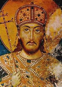 Upper torso and head of a middle-aged bearded man. He wears a domed golden crown, gold-decorated dress and carries a sceptre in the form of a patriarchal cross.