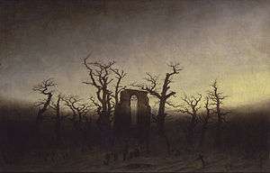 A painting in a yellow and brown palette of a ring of bare tree trunks surrounding a ruined abbey with gravestones on the ground.