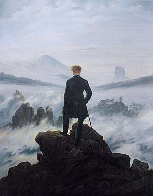 Painting of a man standing with his back to the viewer. He is atop a mountain and surrounded by clouds and fog. He is dressed in black and contrasts sharply with the whites, pinks, and blues of the atmosphere. In the distance outcroppings of rocks can be seen.