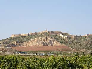 Photo shows a large hill topped with castle walls